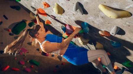 Photo for Athletic Female Rock Climber Practicing Solo Climbing on Bouldering Wall in Gym. Female Exercising at Indoor Fitness Facility, Doing Extreme Sport for Her Healthy Lifestyle Training. Close Up Portrait - Royalty Free Image
