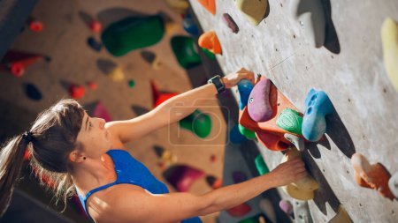 Sportliche Bergsteigerin übt sich im Solo-Klettern an der Boulderwand in der Sporthalle. Frauentraining im Indoor-Fitnessstudio, Extremsport für ihr gesundes Lifestyle-Training. Porträt aus nächster Nähe