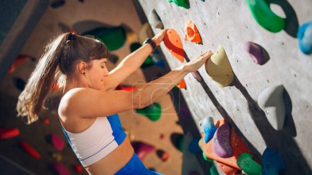 Athletic Female Rock Climber Practicing Solo Climbing on Bouldering Wall in Gym. Female Exercising at Indoor Fitness Facility, Doing Extreme Sport for Her Healthy Lifestyle Training. Close Up Portrait
