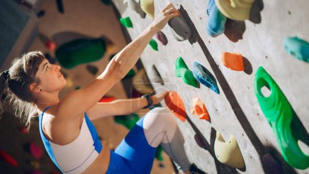 Atlética escaladora femenina practicando escalada en solitario en la pared de Bouldering en el gimnasio. Ejercicio femenino en el gimnasio interior, haciendo deporte extremo para su entrenamiento de estilo de vida saludable. Primer plano Retrato