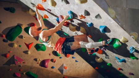 Starker erfahrener Kletterer übt sich im Solo-Klettern an der Boulderwand in der Turnhalle. Mann, der im Indoor-Fitnessstudio Sport treibt, macht Extremsport für sein gesundes Training. Lebensstil-Porträt.