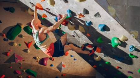 Starker erfahrener Kletterer übt sich im Solo-Klettern an der Boulderwand in der Turnhalle. Mann, der im Indoor-Fitnessstudio Sport treibt, macht Extremsport für sein gesundes Training. Lebensstil-Porträt.
