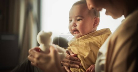 Bonding Moment zwischen Mutter und Baby: Authentische Aufnahme einer Asiatin, die neu in der Mutterschaft ist und morgens zu Hause mit ihrem süßen Kind spielt. Mutter benutzt ein