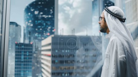 Téléchargez les photos : Homme d'affaires musulman prospère dans l'ascenseur traditionnel en verre blanc Kandura Riding au bureau dans le centre d'affaires moderne. Arabe mâle interagissant avec le faux - en image libre de droit