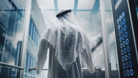 Photo for Successful Happy Muslim Businessman in Traditional White Kandura Riding Glass Elevator to Office in Modern Business Center. Saudi, Emirati, Arab - Royalty Free Image