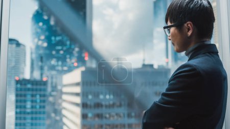 Foto de Elegante empresario japonés montando elevador de cristal a la oficina en el moderno centro de negocios en el centro de Down Town. Joven exitoso asiático macho interacción con - Imagen libre de derechos