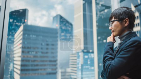 Foto de Elegante empresario japonés montando elevador de cristal a la oficina en el moderno centro de negocios en el centro de Down Town. Joven exitoso asiático macho interacción con - Imagen libre de derechos