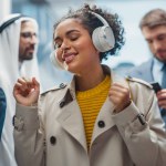 Carefree Black Female Riding Glass Elevator to Office in Modern Business Center. Beautiful Latin Woman is Happy, Smile, Listen to Music on Headphones