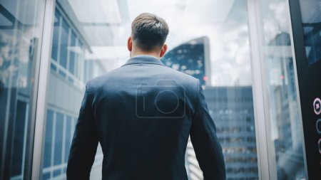 Téléchargez les photos : Homme d'affaires en costume équitation ascenseur en verre au bureau dans le centre d'affaires moderne. Homme regardant les gratte-ciel du centre-ville moderne hors du panorama - en image libre de droit