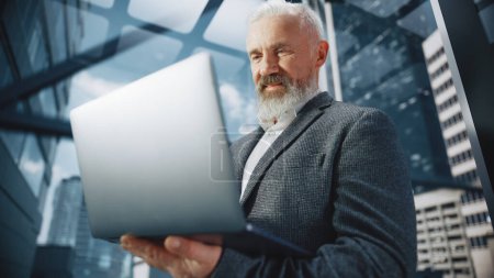 Foto de Exitoso hombre de negocios de mediana edad montando elevador de vidrio a la oficina en el moderno centro de negocios. Hombre feliz guapo usando ordenador portátil, Comprobar horario - Imagen libre de derechos