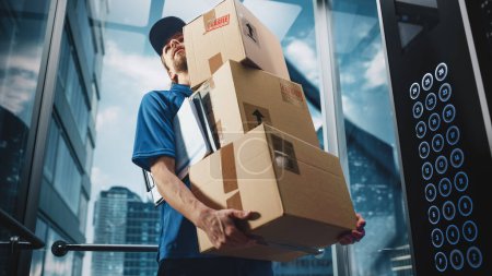 Photo for Young Delivery Person Riding Glass Elevator in Modern Office Building. Mail Courier Holding Cardboard Parcel Boxes. Handsome Mailman Delivering - Royalty Free Image