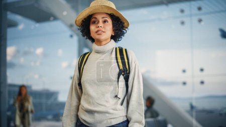 Foto de Terminal del aeropuerto: Mujer negra viajera feliz mira alrededor buscando puertas de vuelo y avión, utiliza Smartphone, Comprobación de destino de viaje en Internet - Imagen libre de derechos