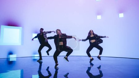 Diverse Gruppe von drei professionellen Tänzern, die eine Hip-Hop-Tanzroutine vor einer großen LED-Wand mit VFX-Animation während einer virtuellen