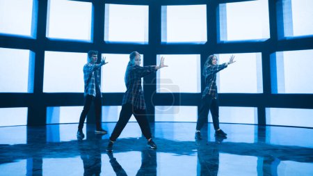 Photo for Diverse Group of Three Professional Dancers Performing a Hip Hop Dance Routine in Front of a Big Led Wall Screen with VFX Animation During a Virtual - Royalty Free Image