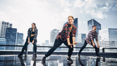 Téléchargez les photos : Groupe diversifié de trois danseurs professionnels effectuant une routine de danse de Hip Hop devant un grand écran mural mené numérique avec la ville moderne Skyline avec - en image libre de droit