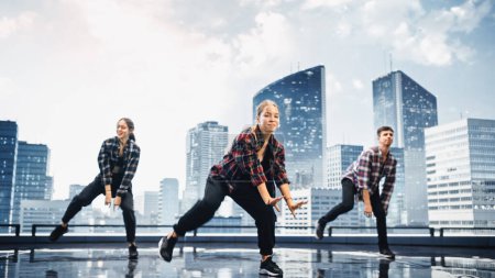 Téléchargez les photos : Groupe diversifié de trois danseurs professionnels exécutant une routine de danse de Hip Hop devant un grand écran mural mené numérique avec l'horizon urbain moderne - en image libre de droit