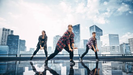 Foto de Diverso grupo de tres bailarines profesionales que realizan una rutina de baile de Hip Hop frente a una gran pantalla de pared led digital con horizonte urbano moderno - Imagen libre de derechos