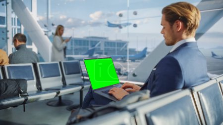 Foto de Terminal del aeropuerto: Empresario que trabaja en el ordenador portátil de pantalla clave de croma verde mientras espera su vuelo en avión. Empresario hace trabajo remoto en línea en - Imagen libre de derechos