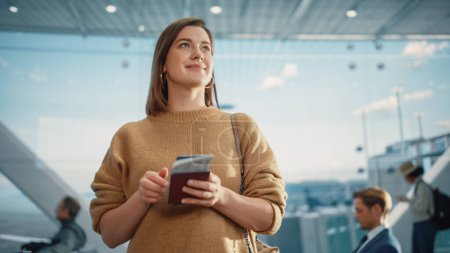 Photo for Airport Terminal: Happy Traveling Caucasian Woman Waiting at Flight Gates for Plane Boarding, Uses Mobile Smartphone, Checking Trip Destination on - Royalty Free Image
