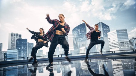 Photo for Diverse Group of Three Professional Dancers Performing a Hip Hop Dance Routine in Front of a Big Digital Led Wall Screen with Modern Urban Skyline - Royalty Free Image