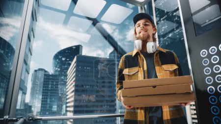 Photo for Young Handsome Specialist Riding Glass Elevator in Modern Office Building. Restaurant Delivery Courier Holding Take Away Pizza Boxes. Handsome - Royalty Free Image