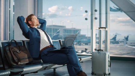 Foto de Terminal del aeropuerto: Empresario utiliza ordenador portátil, esperando para el vuelo. Traveling Man Relax after Work, Mirando hacia adelante a las vacaciones. Sentado en un - Imagen libre de derechos