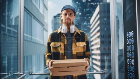 Photo for Young Handsome Food Delivery Person Riding Glass Elevator in Modern Office Building. Restaurant Delivery Courier Holding Take Away Pizza Boxes - Royalty Free Image