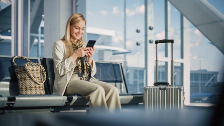 Téléchargez les photos : Aérogare : Woman Waits for Flight, Utilise Smartphone, Parcourir Internet, Médias sociaux, Achats en ligne. Travail à distance féminin itinérant en ligne sur - en image libre de droit