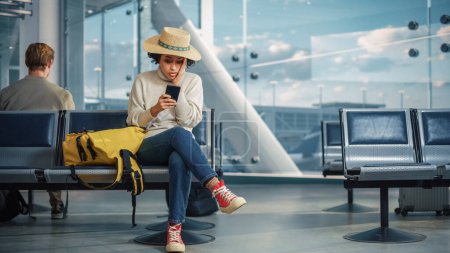 Téléchargez les photos : Terminal de l'aéroport : Black Woman Waits for Flight, utilise un smartphone, reçoit des mauvaises nouvelles choquantes, rate le vol. Perturbations, tristesse et déception - en image libre de droit
