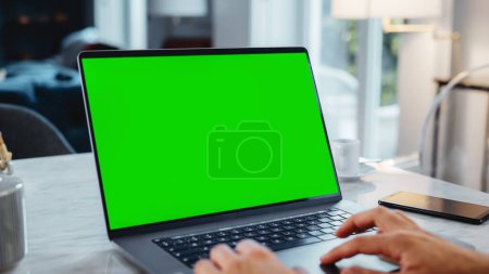 Téléchargez les photos : Affichage maquillé d'écran vert sur un ordinateur portable. Gros plan sur les personnes qui travaillent de la maison moderne, qui utilisent le pavé tactile, qui font défiler le contenu. Smartphone - en image libre de droit