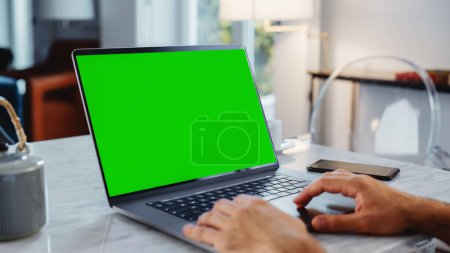 Green Screen Mock Up Display on a Laptop Computer. Close Up on Persons Hands Working from Modern Home, Using Touch Pad, Scrolling Content. Smartphone