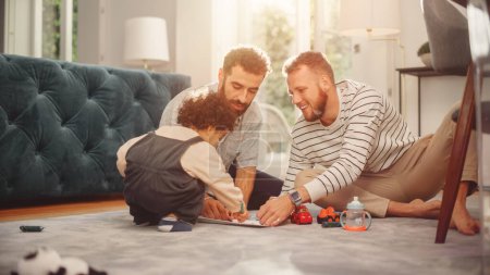 Téléchargez les photos : Aimer la famille LGBTQ Jouer avec des jouets avec Adorable bébé garçon à la maison sur le plancher du salon. Couple gai gai qui élève un enfant. Concept de diversité - en image libre de droit