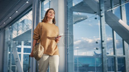 Téléchargez les photos : Terminal de l'aéroport : Belle femme souriante détient un billet, marche à travers Big Airline Hub jusqu'aux portes où son avion l'attend. heureux caucasien - en image libre de droit