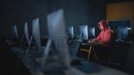 Téléchargez les photos : Étudiant masculin concentré assis seul dans la salle informatique du collège, soirée de travail sur le projet informatique. Jeune érudit Étude IT sur - en image libre de droit