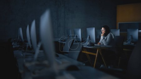 Téléchargez les photos : Jeune étudiante musulmane assise seule dans la salle informatique du collège, travaillant tard le soir sur le projet informatique. Étude érudite IT sur ordinateur - en image libre de droit