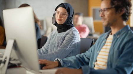 Foto de Estudiante musulmana curiosa que usa un hiyab, estudia en la Universidad Moderna con diversos compañeros de clase multiétnicos. Estudiantes universitarios trabajan en la universidad - Imagen libre de derechos