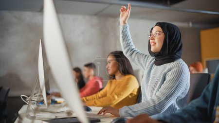 Téléchargez les photos : Étudiante musulmane intelligente à Hijab Étudier à l'université avec divers camarades de classe multiethniques. Elle lève la main et pose une question au professeur. Application - en image libre de droit