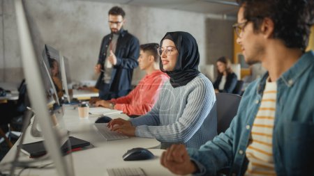 Téléchargez les photos : Étudiante musulmane portant le hijab, étudiant à l'université moderne avec divers camarades de classe multiethniques. Elle pose une question au chercheur dans la salle du collège - en image libre de droit