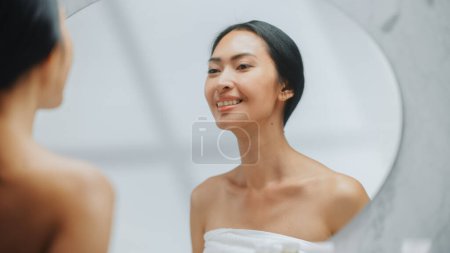 Téléchargez les photos : Portrait de belle femme asiatique vérifiant ses dents blanches naturelles propres, sourires dans miroir de salle de bains. Joyeuse Femme Profitant de la routine du matin. Soins dentaires - en image libre de droit