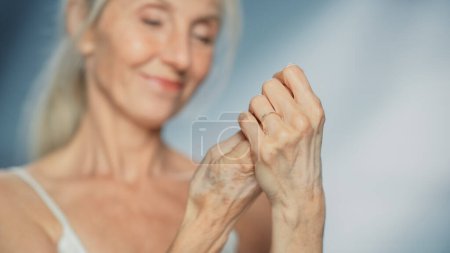 Porträt einer schönen Seniorin, die Handcreme benutzt. Ältere Dame macht ihre Haut weich, glatt, faltenfrei mit natürlichem Anti-Aging