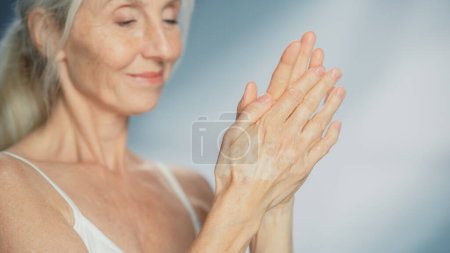 Porträt einer schönen Seniorin, die Handcreme benutzt. Ältere Dame macht ihre Haut weich, glatt, faltenfrei mit natürlichem Anti-Aging