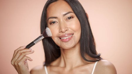 Téléchargez les photos : Portrait de beauté féminine. Belle femme brune asiatique multiethnique heureuse utilisant le pinceau de maquillage Blush dans le bien-être, les cosmétiques, le spa et les soins de la peau naturels - en image libre de droit