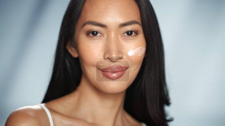 Retrato de belleza femenina. Hermosa mujer asiática sonriente con piel natural y saludable, ha aplicado crema facial nutritiva en ella. Cosméticos y Dermatología
