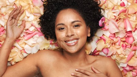 Photo for Female Beauty Portrait Lying in Flower Bed. Sensual Black Multiethnic Woman with Afro Hair, Natural, Clean, Healthy Skin Posing and Smiling. Wellness - Royalty Free Image