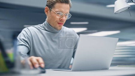 Photo for Modern Office: Productive Businessman Sitting at His Desk Working on a Laptop Computer. Man working with Big Data e-Commerce Analysis. Energetic Shot - Royalty Free Image