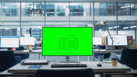 Foto de Monitor de computadora de escritorio con pantalla verde simulada Pantalla clave de croma de pie en el escritorio de la oficina de negocios moderna. En la pared de cristal de fondo - Imagen libre de derechos