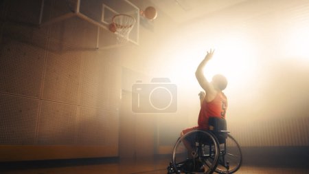 Téléchargez les photos : Joueur de basketball en fauteuil roulant portant une balle de tir uniforme rouge avec succès, marquant un objectif parfait. Détermination, formation, inspiration d'une personne - en image libre de droit
