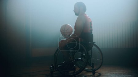 Téléchargez les photos : Portrait d'un joueur de basketball en fauteuil roulant tenant un ballon, s'entraînant. Détermination, formation, inspiration des personnes handicapées. Tourné avec des couleurs froides - en image libre de droit