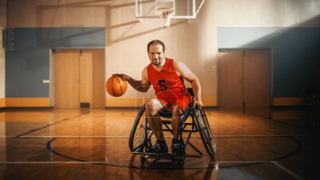 Photo for Portrait of Handsome Wheelchair Basketball Player Wearing Red Shirt Dribbling Ball, Looking at Camera and Smiling. Determined, Motivativated Person - Royalty Free Image