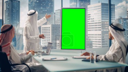 Téléchargez les photos : Emirati Businessman organise une présentation de réunion pour les partenaires commerciaux. Arab Manager utilise le tableau blanc numérique avec écran vert vertical Mock Up Display - en image libre de droit